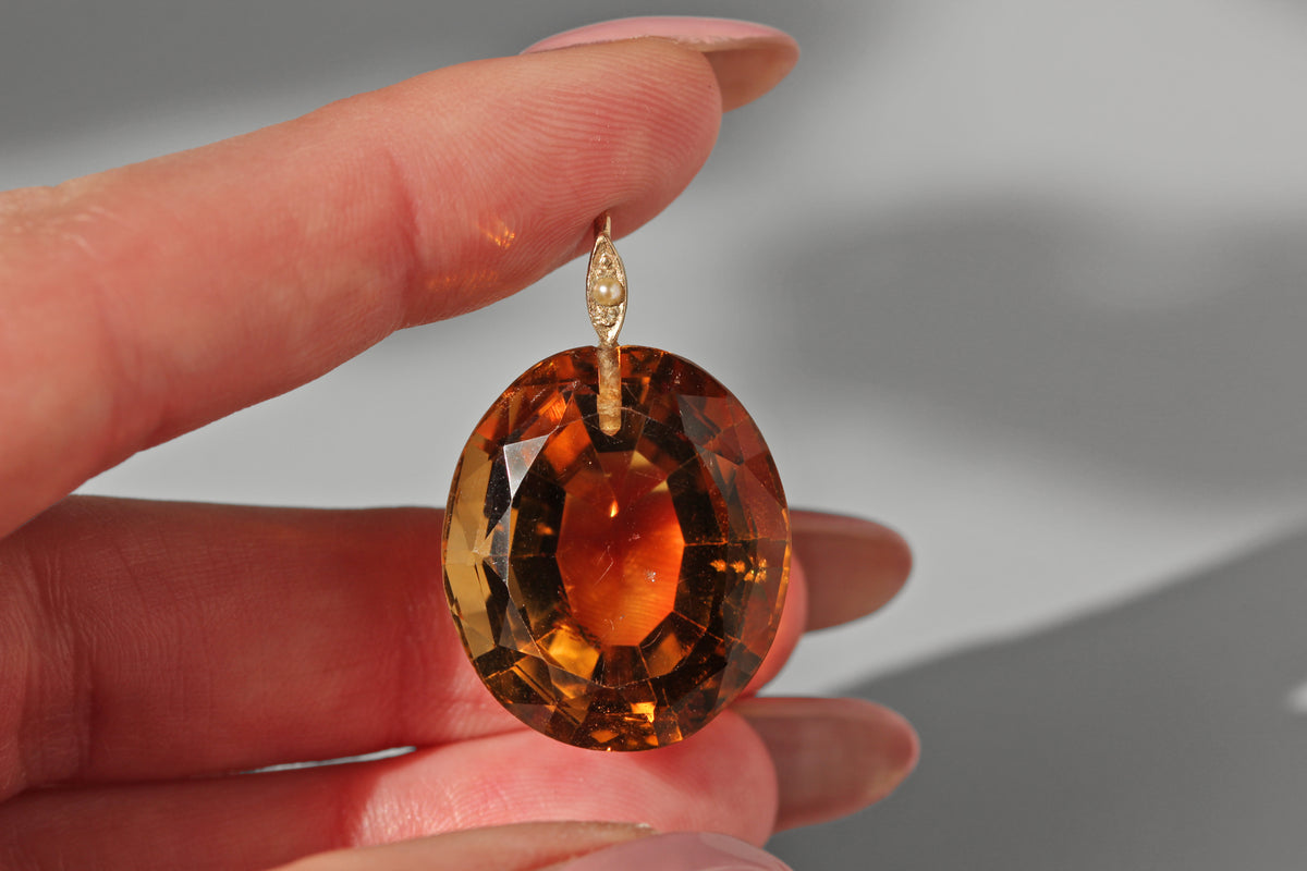 a hand holding a large citrine gemstone with a 9ct gold mount set with a seed pearl 
