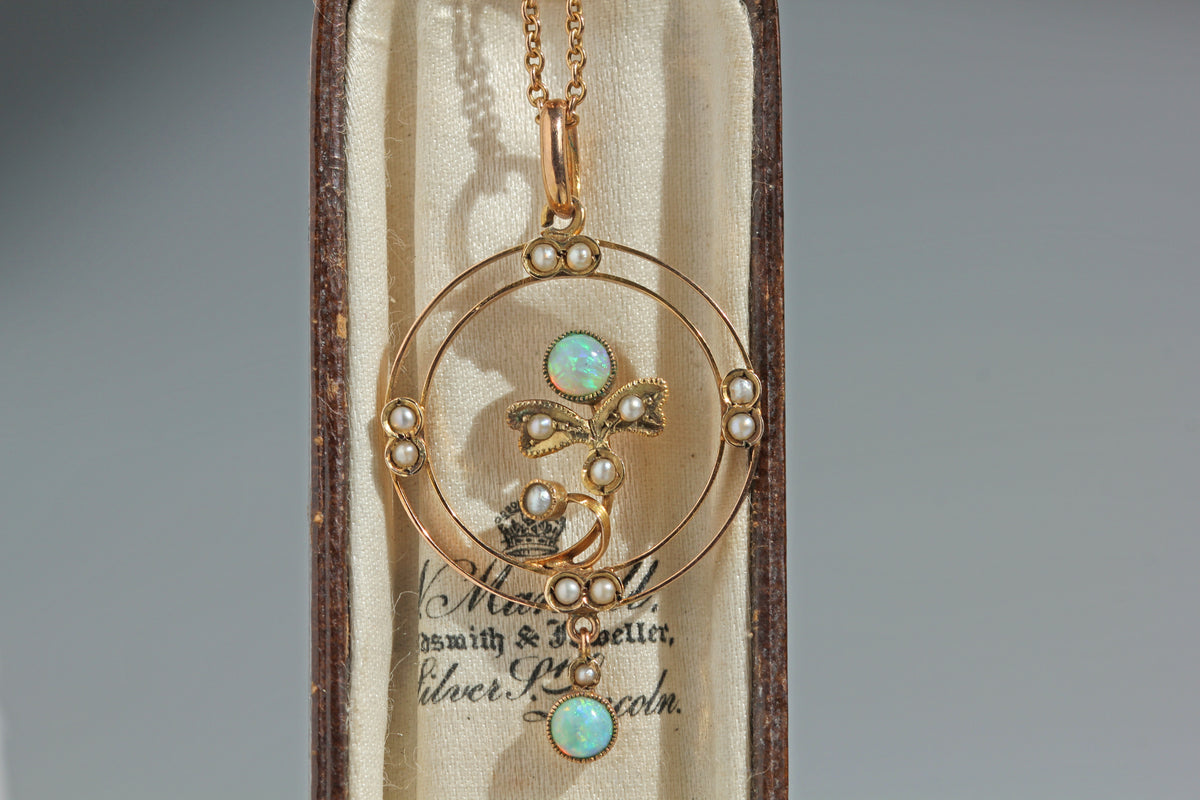 An antique 9ct gold pendant necklace with opal and pearl accents with a floral feature, displayed inside original wooden presentation box with a cream satin lining.