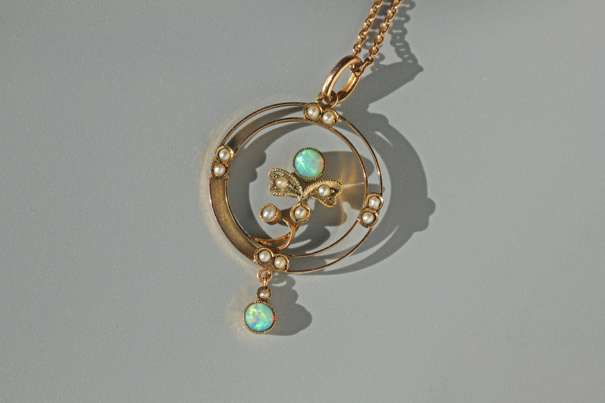 A 9ct gold antique pendant necklace featuring a circular openwork design, small pearl beads, and two iridescent opal gemstones, displayed on a neutral gray background.