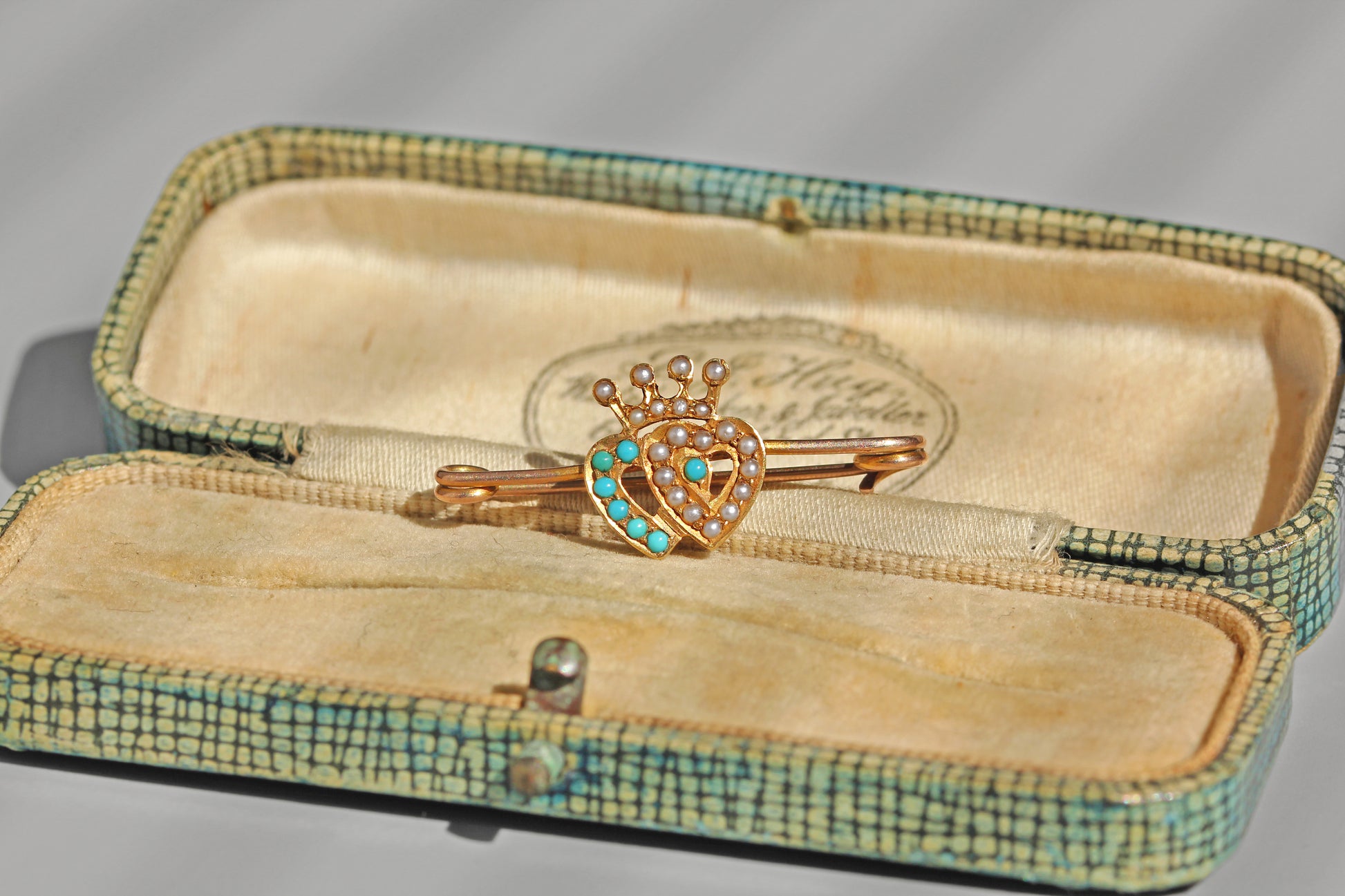 Antique turquoise and pearl double heart brooch in 15ct gold resting on a blue antique jewellery box

