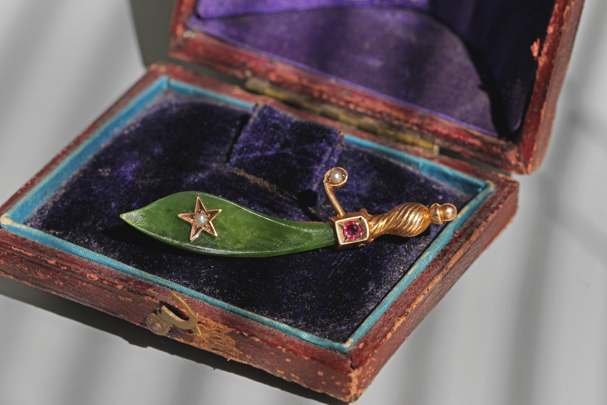 Antique jade and ruby brooch resting inside a purple velvet jewellery box

