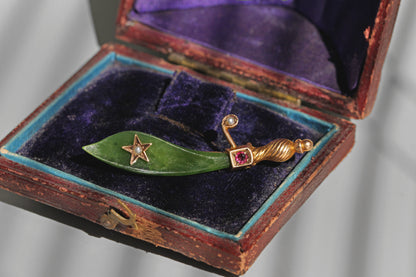 Antique jade and ruby brooch resting inside a purple velvet jewellery box
