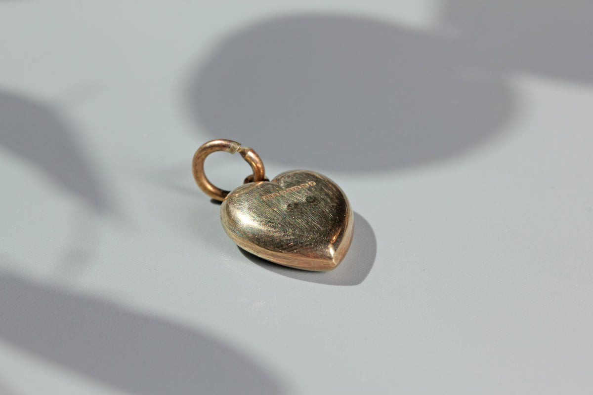 Heart-shaped gold charm on a light gray background