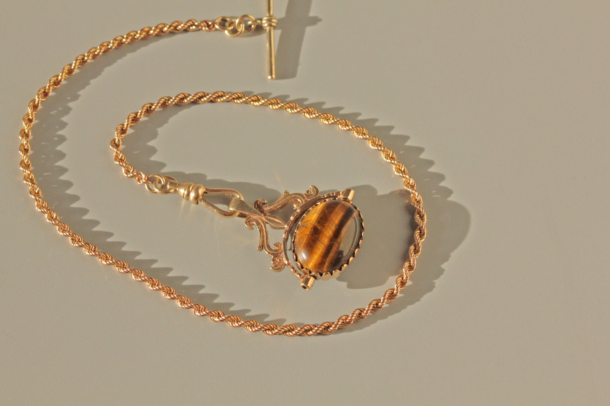 Gold necklace with a tiger's eye stone on a beige background