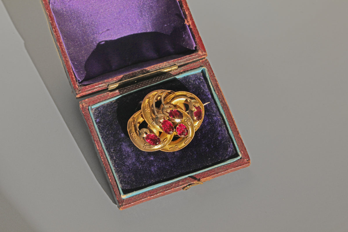 Gold and red gemstone brooch in an open jewelry box on a gray background