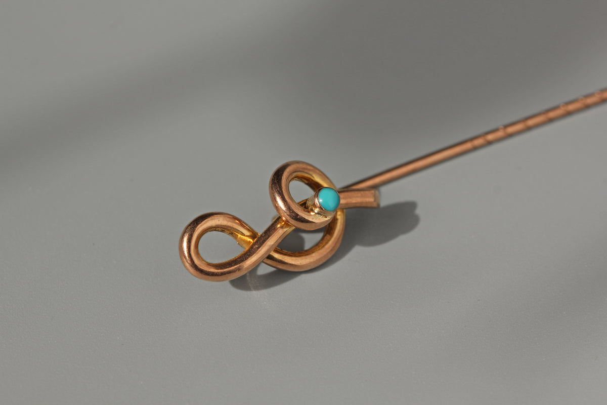 A 9ct rose gold musical pin with a decorative treble clef design and a small turquoise stone accent, shown on a neutral gray background.