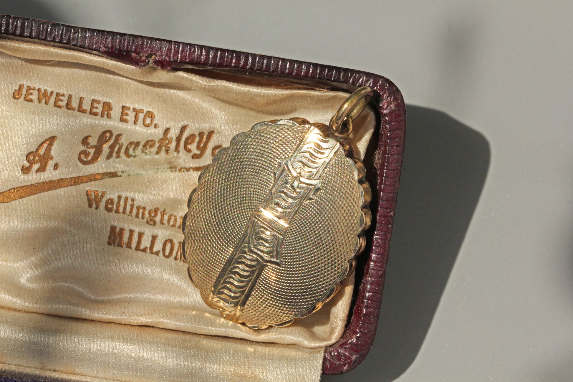 Antique gold locket with scalloped edge and symbolic buckle motif
