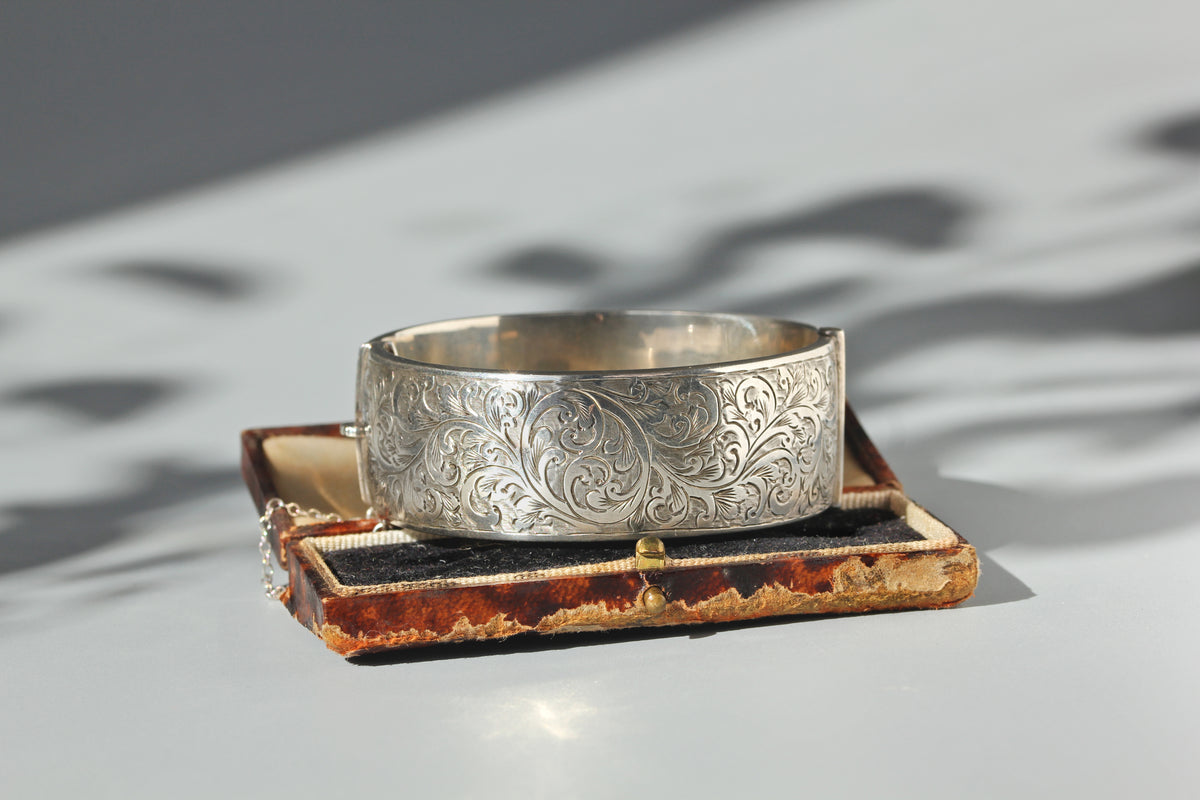 Vintage sterling silver engraved hinged cuff bangle with etched foliate details and original safety chain, displayed in antique jewellery box