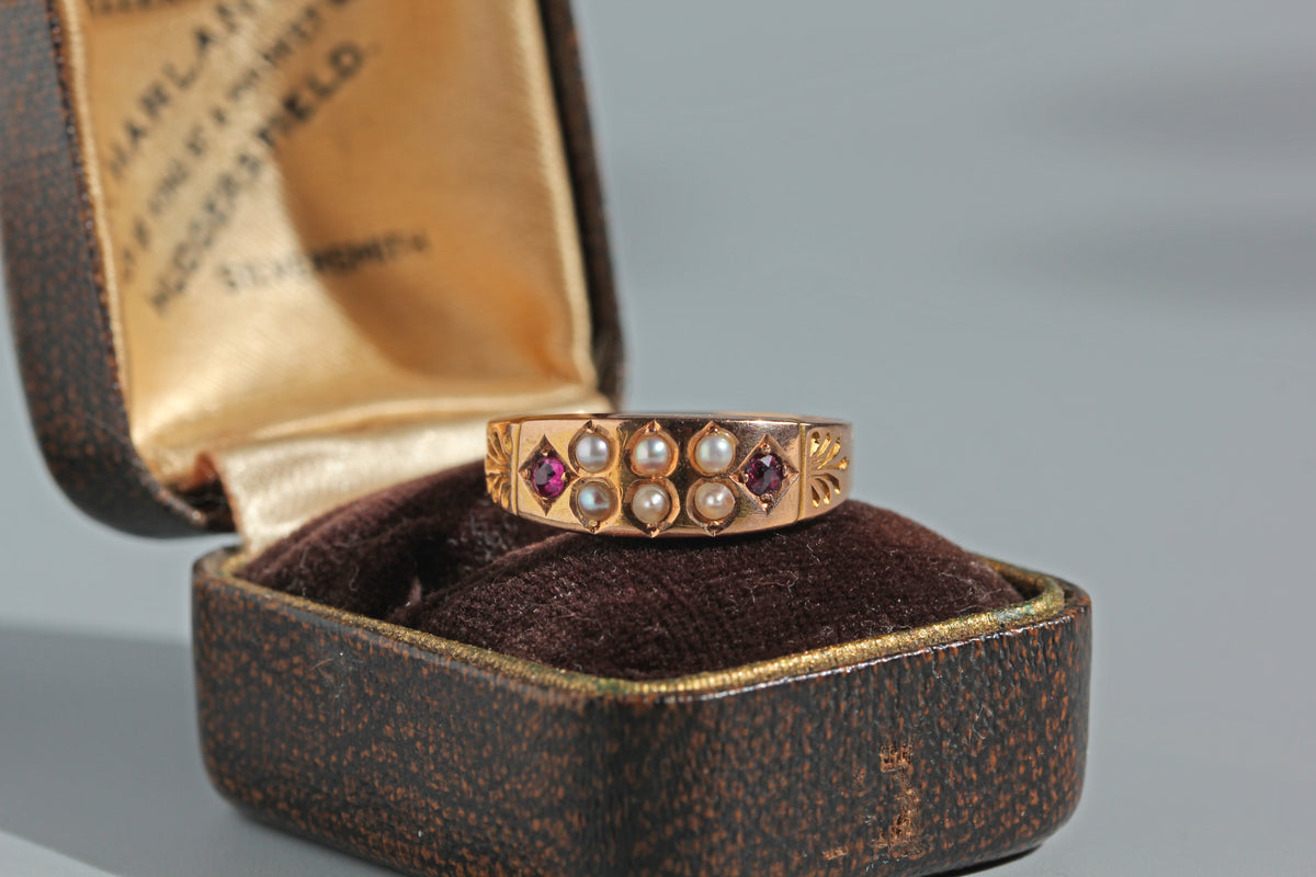 An antique 15ct gold victorian ring, decorated with six pearls and two pink rubies, displayed on an antique ring box