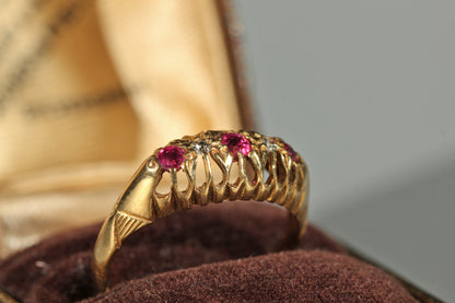 A close-up of the openwork gallery on an antique 18ct gold boat ring with pink rubies and old cut diamonds, displayed in a brown velvet jewelry box.