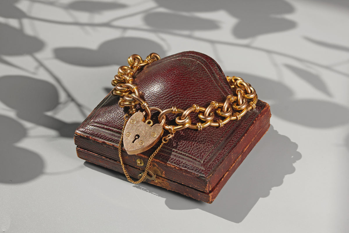 Antique fancy link heart padlock bracelet in 9ct gold, displayed on a leather jewellery box
