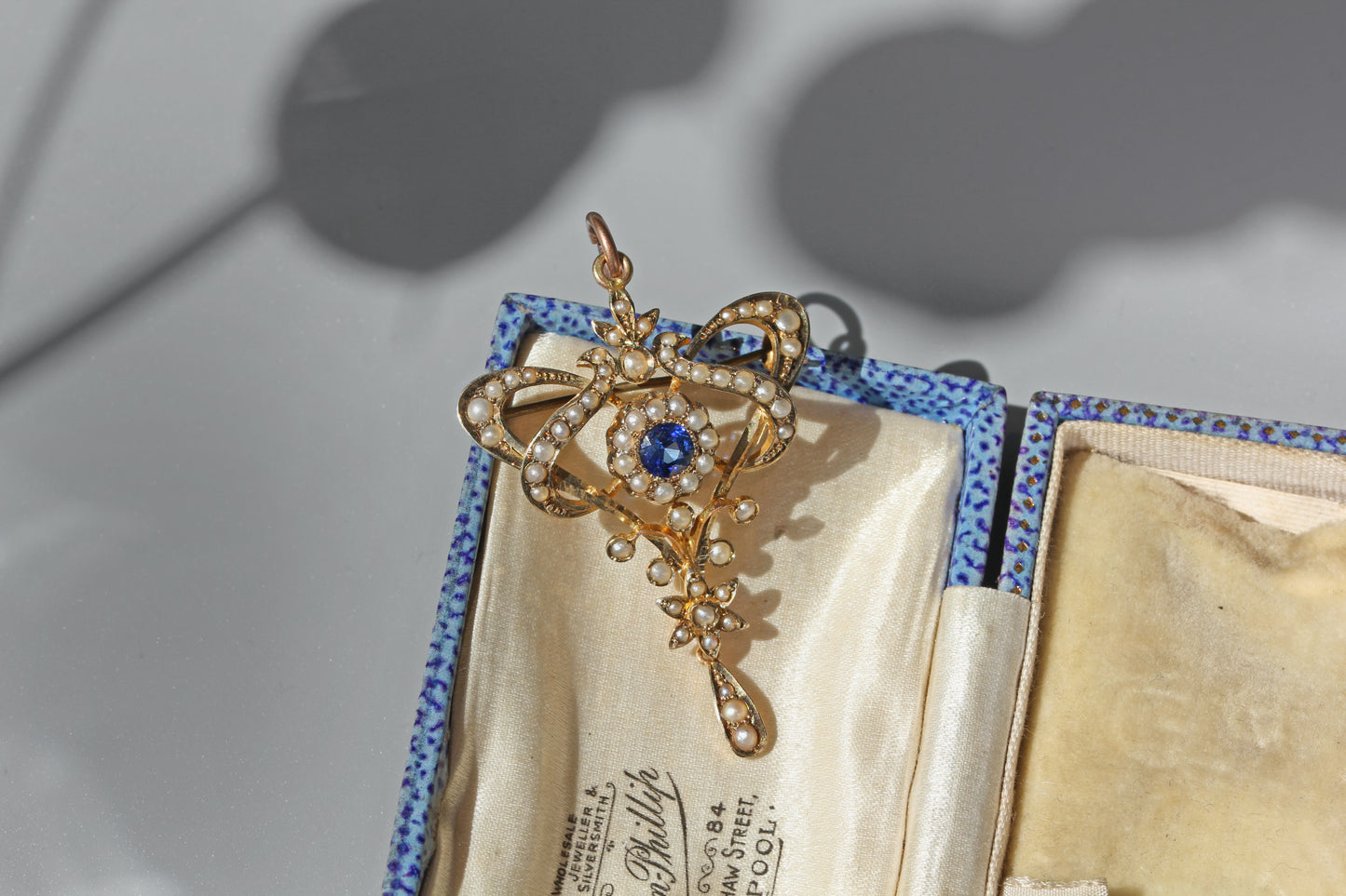 Close up of antique blue paste and pearl pendant showing floral drop and ribbon design
