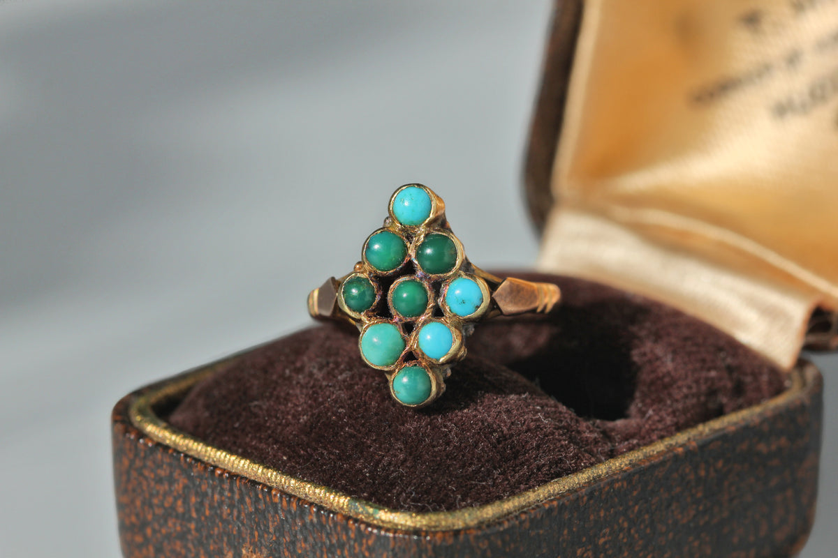 An antique 9ct gold ring with a cluster of turquoise cabochon stones in a navette or lozenge shape, displayed in an open antique jewelry box with a dark brown velvet lining.