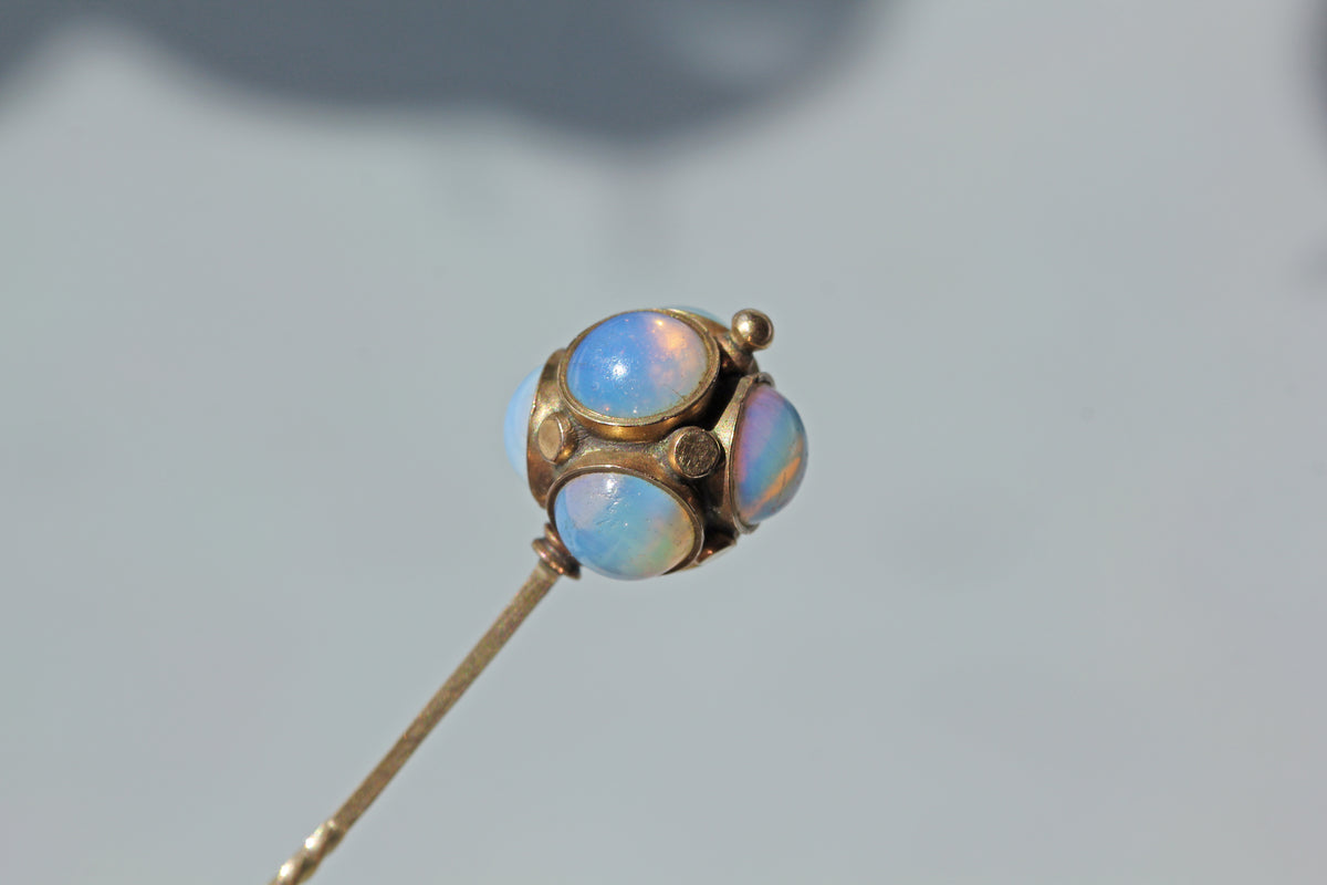 An antique 9ct gold stick pin, featuring a celestial orb of milky iridescent opals and gold studs, displayed on neutral grey background 