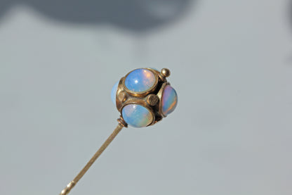An antique 9ct gold stick pin, featuring a celestial orb of milky iridescent opals and gold studs, displayed on neutral grey background 