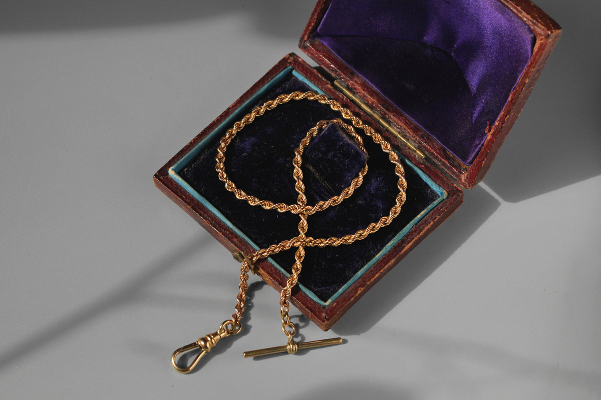 antique 9ct gold watch chain with rope link and dog clip, displayed on vintage jewellery box