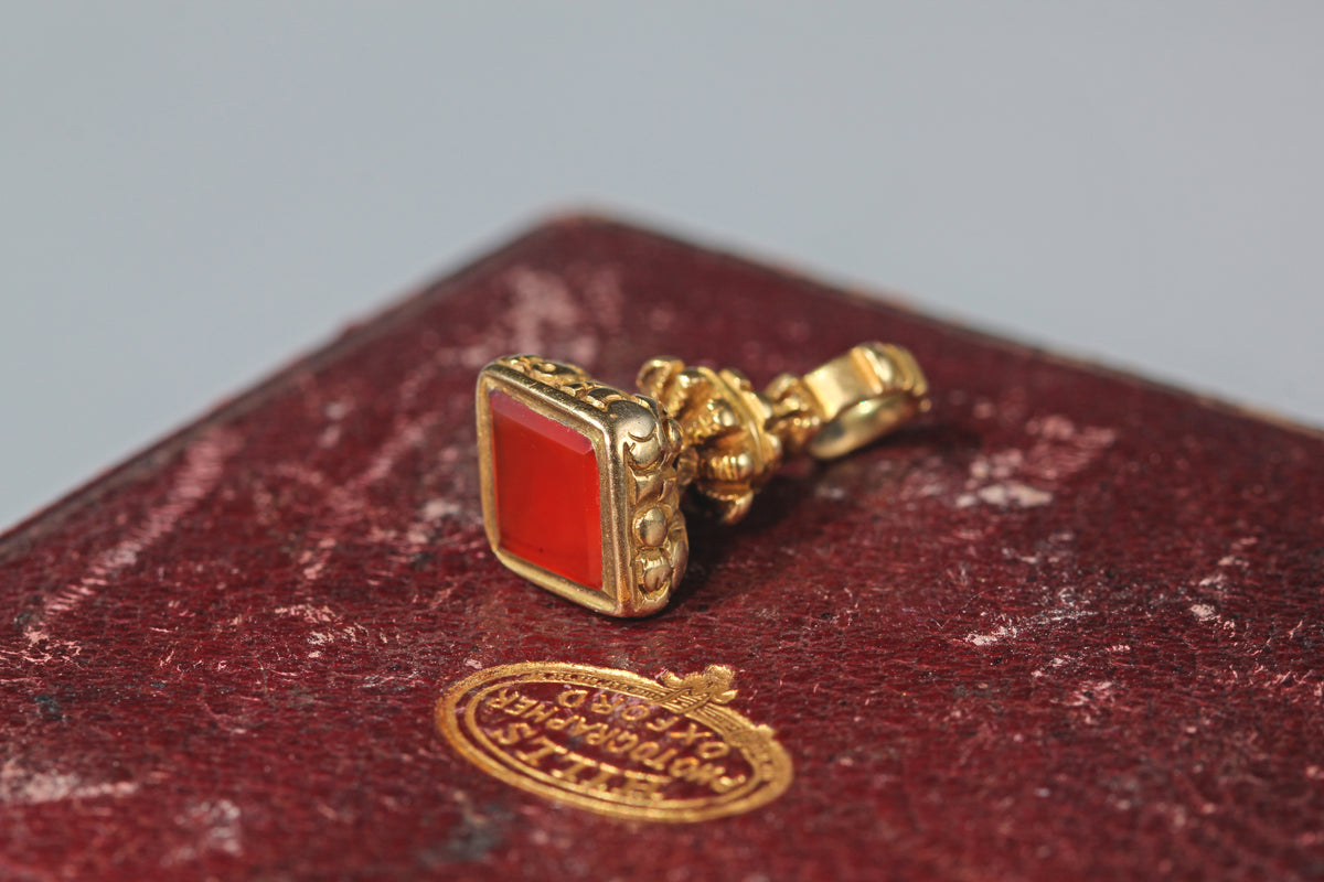 Antique 9ct gold carnelian fob seal pendant in a lozenge shape, displayed on antique jewellery box