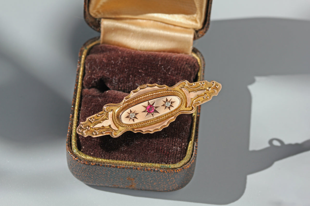 Antique 9ct gold victorian brooch with pink ruby spinel and diamonds set in celestial bezels, with ornate details and a unique silhouette, displayed on an antique ring box