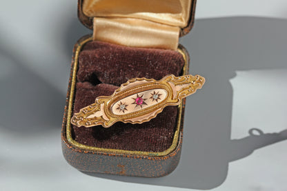 Antique 9ct gold victorian brooch with pink ruby spinel and diamonds set in celestial bezels, with ornate details and a unique silhouette, displayed on an antique ring box