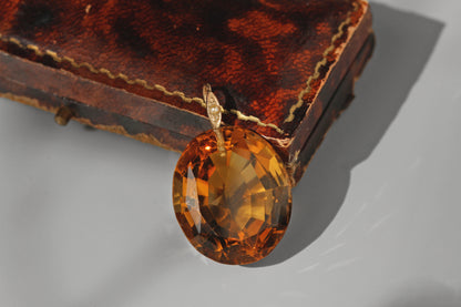 A large antique faceted citrine gemstone, with a 9ct gold mount set with a seed pearl displayed on an antique jewellery box