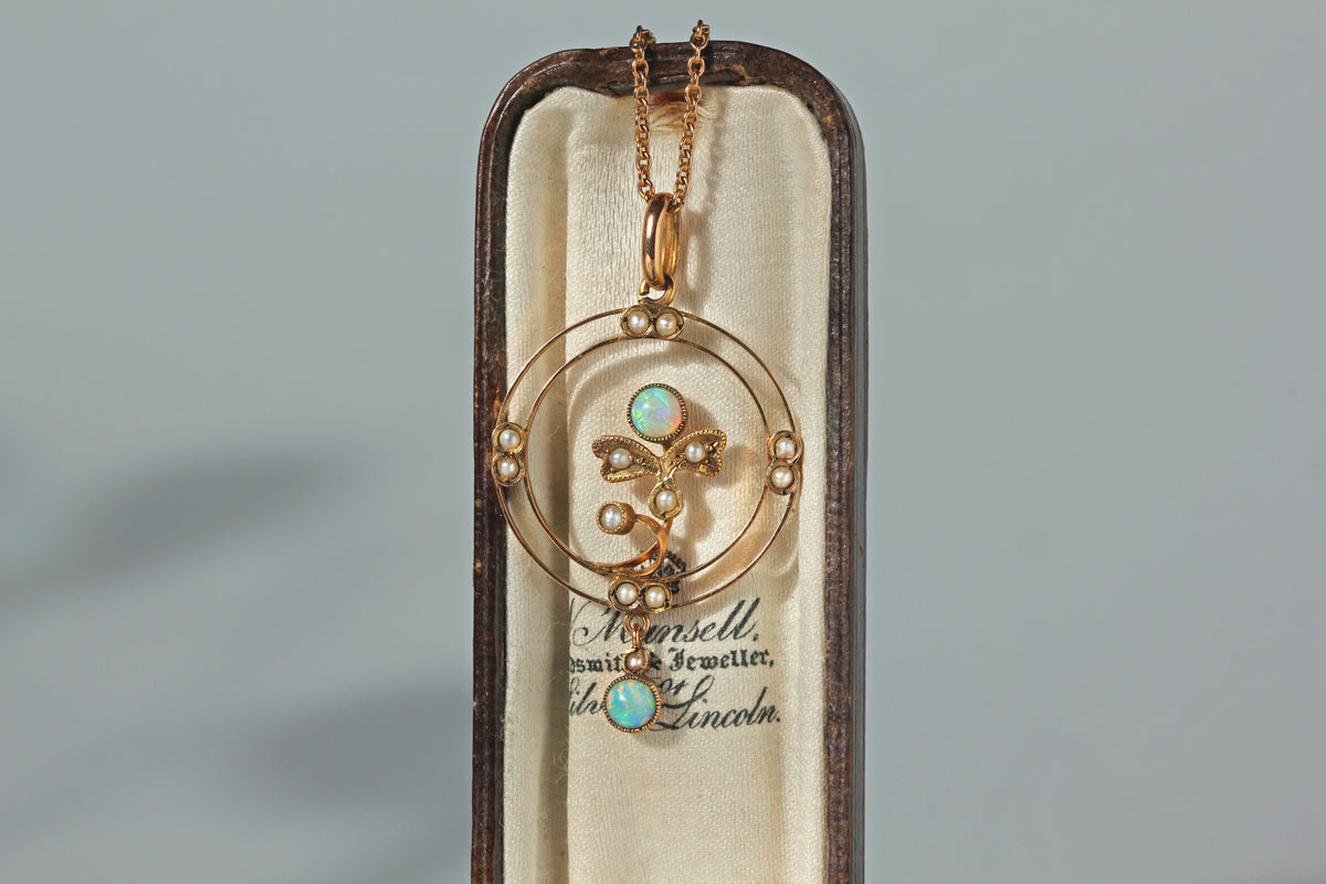 An antique 9ct gold edwardian opal and pearl pendant necklace, with an openwork frame and a floral formation in the centre, displayed in an antique jewellery box