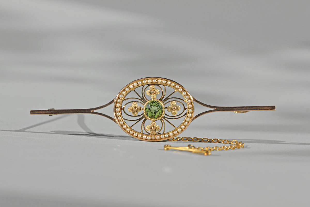 Antique edwardian 9ct gold brooch with safety chain, featuring a peridot, stylised flower motifs and a halo of seed pearls