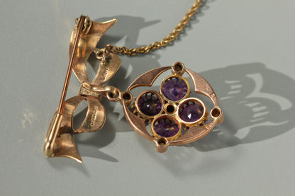 A close up of the back of a vintage 9ct gold brooch pendant, with lear hallmarks and the details of four round cut amethysts, displayed on neutral grey background 