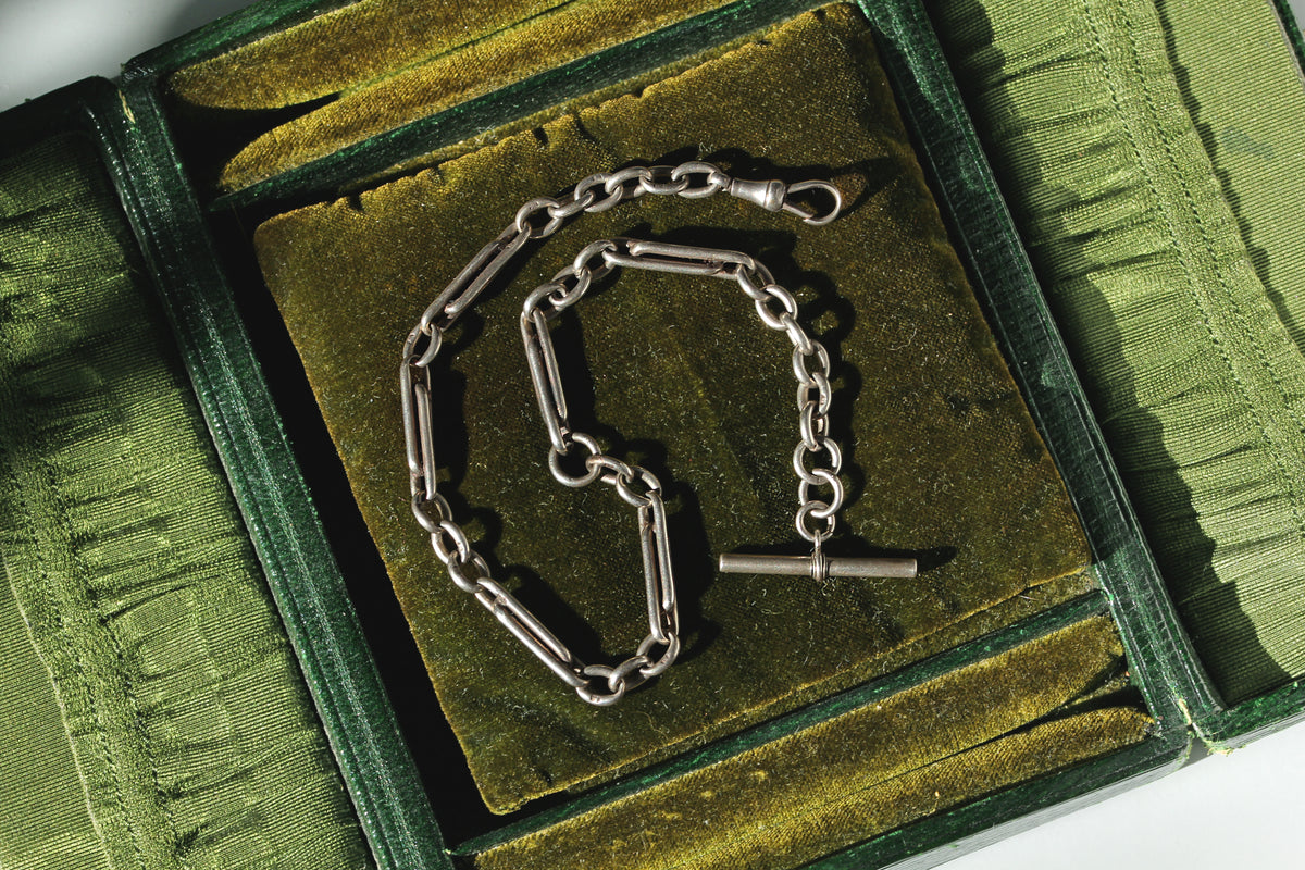 Antique 925 sterling silver trombone or paperclip link Albert watch chain with dog clip and t bar, displayed on antique jewellery box