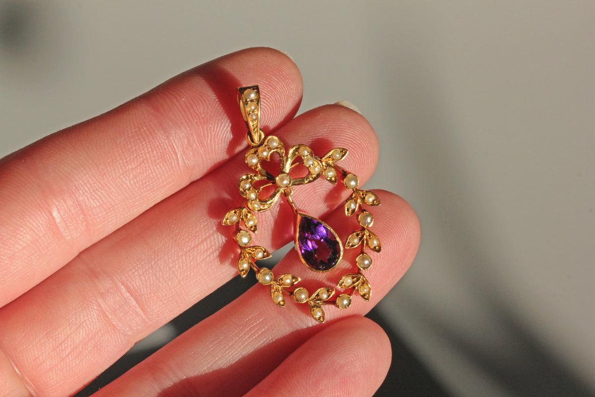 Hand holding an antique victorian seed pearl and pear cut amethyst stone pedant, in 9ct gold