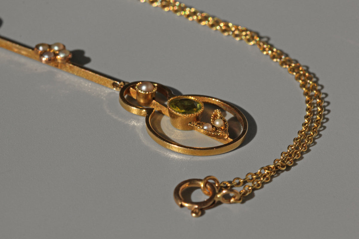 close up of gold necklace with a pendant featuring a green gemstone on a gray background