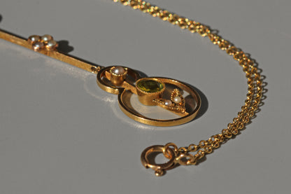 close up of gold necklace with a pendant featuring a green gemstone on a gray background