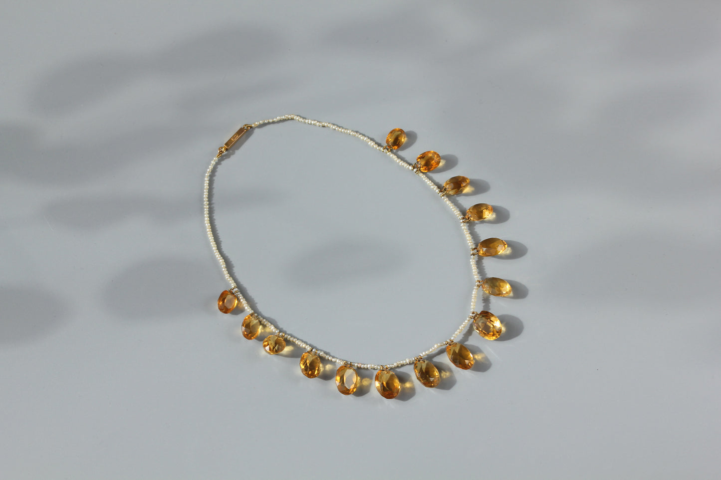A 15ct gold chain necklace featuring a row of citrine gemstones amongst hand strung pearls, displayed on a neutral gray background with soft shadows.