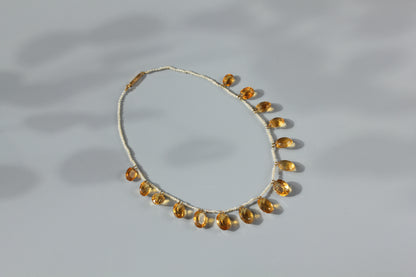 A 15ct gold chain necklace featuring a row of citrine gemstones amongst hand strung pearls, displayed on a neutral gray background with soft shadows.