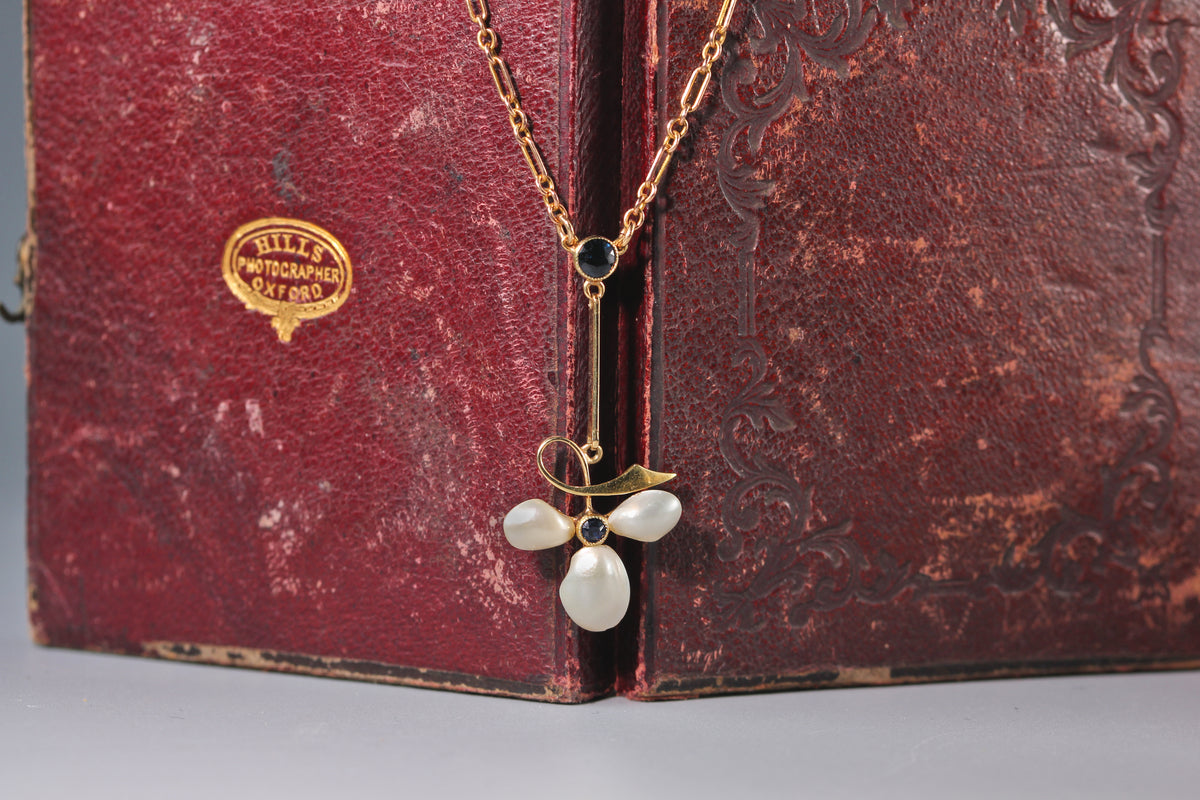 Antique 15ct gold necklace with sapphires and pearls in the form of a clover of ivy leaf, displayed on antique jewellery box