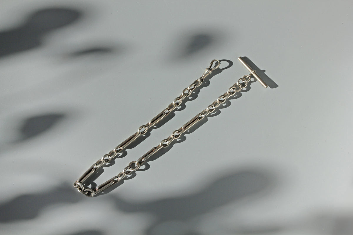 Sterling silver antique watch chain with trombone or paperclip links, with a dog clip and t-bar photographed on a grey background