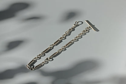 Sterling silver antique watch chain with trombone or paperclip links, with a dog clip and t-bar photographed on a grey background