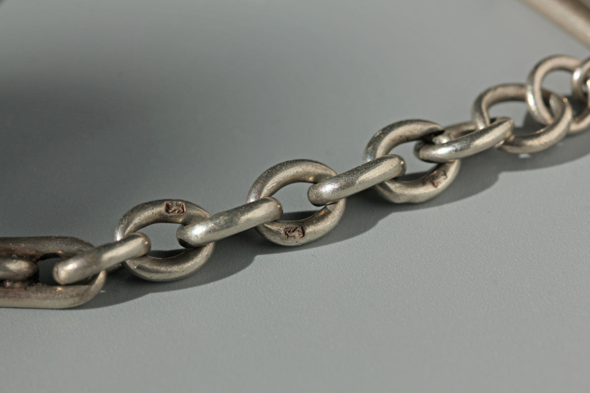 A close-up of a sterling silver metal chain lion passant hallmarks with interlocking oval links on a smooth gray surface.