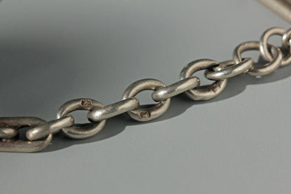 A close-up of a sterling silver metal chain lion passant hallmarks with interlocking oval links on a smooth gray surface.