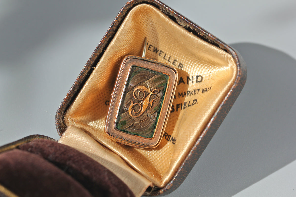 An antique victorian hairwork mourning brooch crafted in 9ct gold with a monogram initial letter 'F', displayed in an antique ring box