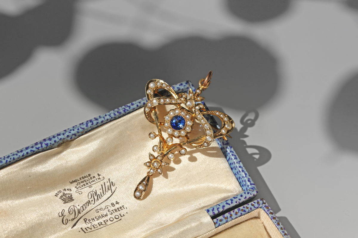 Antique blue paste and seed pearl lavaliere pendant in 9 carat gold resting on an antique jewellery box