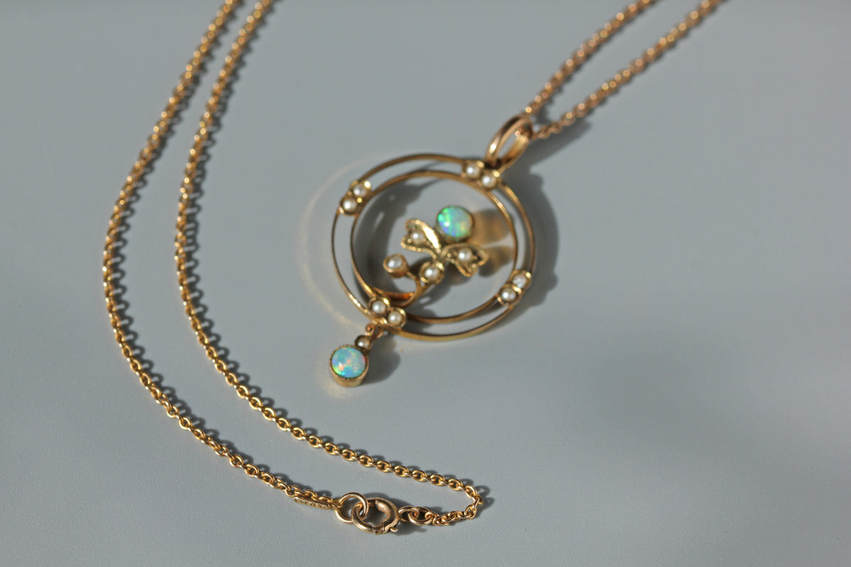 A 9ct gold cable chain necklace with a circular pendant featuring a central floral motif, small pearls, and two iridescent opal gemstones, displayed on a light gray background.