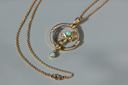 A 9ct gold cable chain necklace with a circular pendant featuring a central floral motif, small pearls, and two iridescent opal gemstones, displayed on a light gray background.