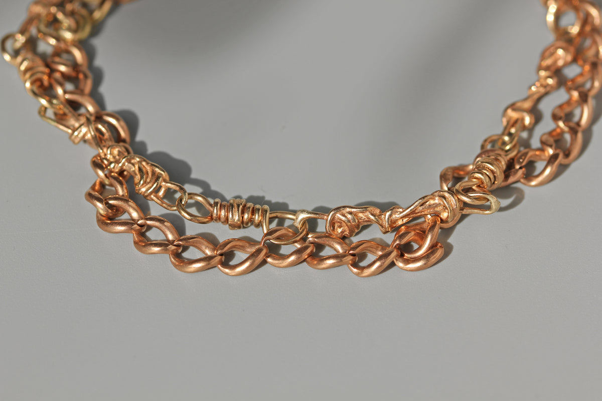 A close-up of 9ct chain bracelet with twisted and knotted link details, resting on a neutral gray background.