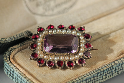 Close up details of cushion cut amethyst in collet setting with pearls and garnets, in an antique jewellery box 