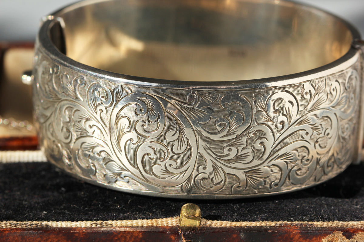 An ornate silver-toned cuff bracelet with intricate floral engraving, displayed on a dark velvet jewelry box.