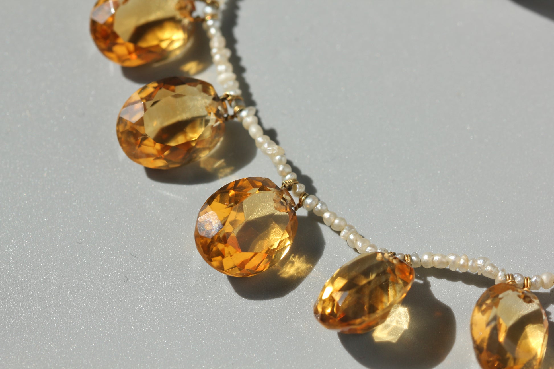 A close-up of an antique beaded necklace featuring faceted citrine stones and small white pearls on a light gray background