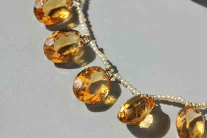 A close-up of an antique beaded necklace featuring faceted citrine stones and small white pearls on a light gray background