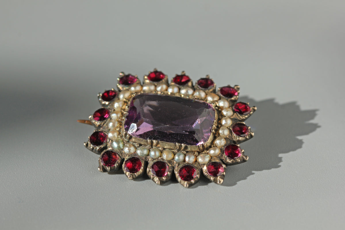 Georgian 9ct gold brooch with pearls, amethyst and garnets on a grey background 