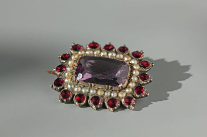 Georgian 9ct gold brooch with pearls, amethyst and garnets on a grey background 