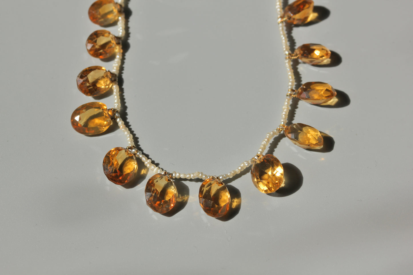 Close up of faceted golden citrine drops and tiny seed pearls on antique fringe necklace